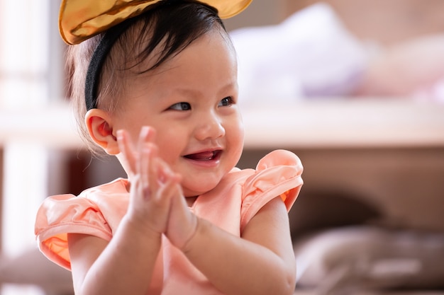 Nettes asiatisches Baby, das lächelt und ihre Hand klatscht, während sie mit ihren Eltern im Wohnzimmer spielt.