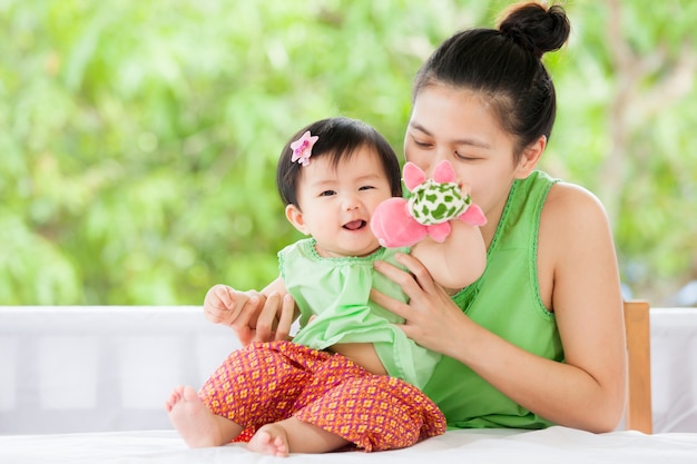 Nettes asiatisches Baby, das mit ihrer Mutter- und Schildkrötenpuppe lächelt und spielt