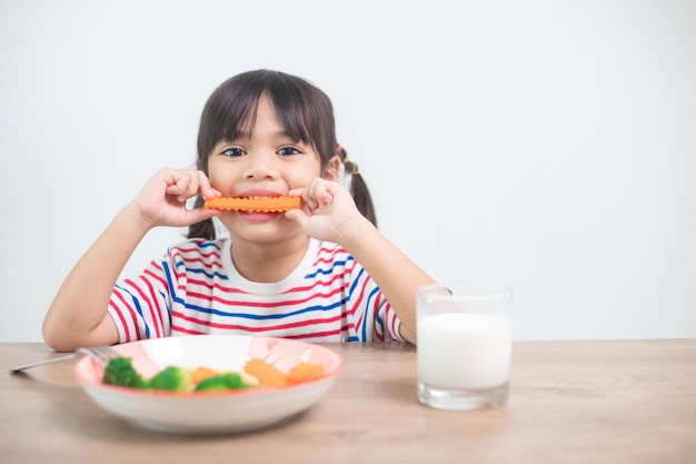 Nettes asiatisches Kindermädchen, das gesundes Gemüse und Milch für ihre Mahlzeit isst