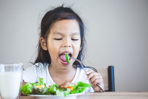 Nettes asiatisches Kindermädchen, das gesundes Gemüse und Milch für ihre Mahlzeit isst