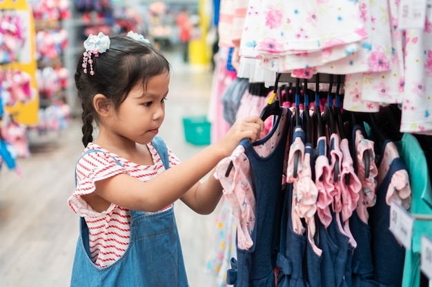 Nettes asiatisches Kindermädchen, das Kleider in der Kleidungsabteilung im Supermarkt wählt