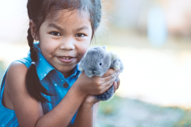 Nettes asiatisches Kindermädchen, das mit kleinem Häschen mit Liebe und Weichheit spielt