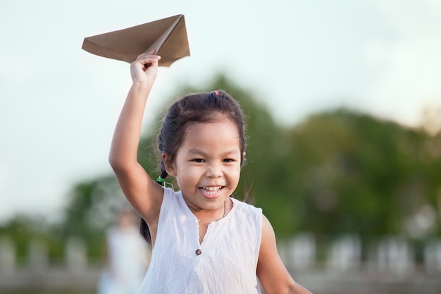 Nettes asiatisches Kindermädchen, das Spielzeugpapierflugzeug auf dem Gebiet im Weinlesefarbton läuft und spielt