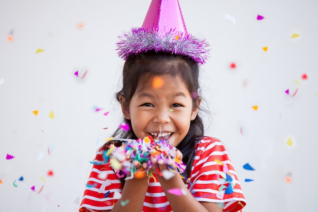 Nettes asiatisches Kindermädchen mit den bunten Konfettis, zum in ihrer Party zu feiern