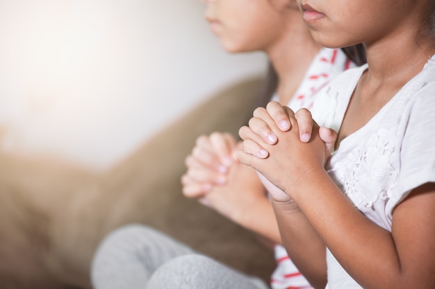 Nettes asiatisches Kindermädchen und ihre Schwester, die mit zusammen betet, faltete ihre Hand im Raum zusammen