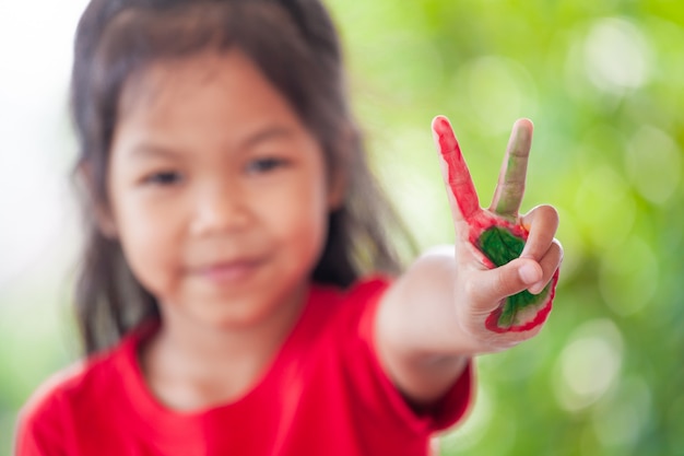 Nettes asiatisches kleines Kindermädchen mit den gemalten Händen, die Finger Nummer zwei zeigen