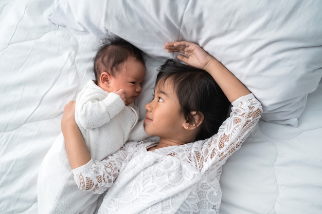 Nettes asiatisches Mädchen, das mit seinem kleinen Bruder auf dem Bett liegt