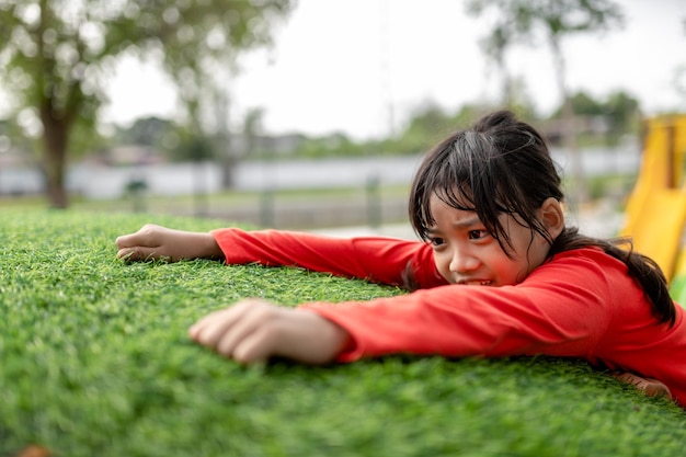 Nettes asiatisches Mädchen, das Spaß daran hat, auf künstlichen Felsbrocken auf dem Schulhofspielplatz zu klettern Kleines Mädchen, das die Felswand hinaufklettert Entwicklung der Hand-Augen-Koordinationsfähigkeiten