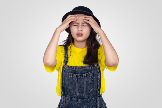 Nettes asiatisches Mädchen im gelben Schwindel und Kopfschmerzen mit weißem Hintergrund
