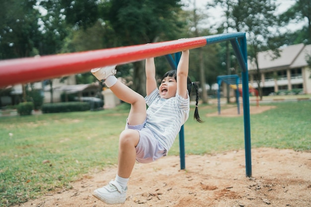 Nettes asiatisches Mädchen spielen auf Schul- oder Kindergartenhof oder Spielplatz Gesunde Sommeraktivität für Kinder Kleines asiatisches Mädchen, das draußen auf dem Spielplatz klettert Kind spielt auf dem Spielplatz im Freien