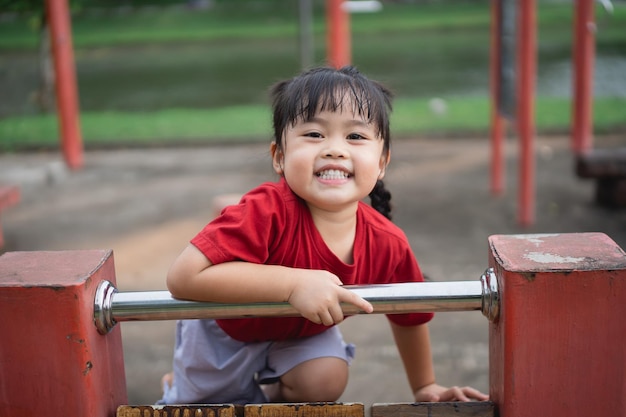 Nettes asiatisches Mädchen spielen auf Schul- oder Kindergartenhof oder Spielplatz Gesunde Sommeraktivität für Kinder Kleines asiatisches Mädchen, das draußen auf dem Spielplatz klettert Kind spielt auf dem Spielplatz im Freien