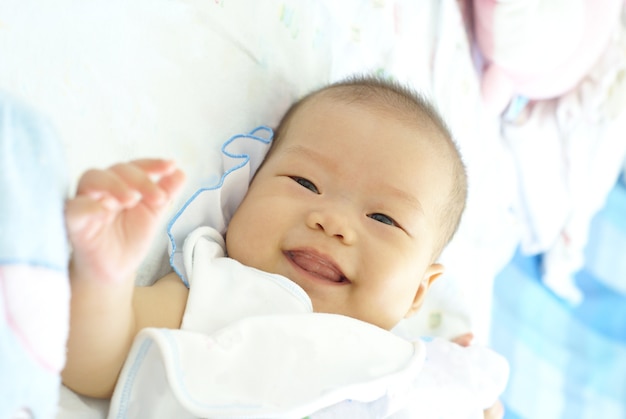 Nettes asiatisches Säuglingsbaby im weißen Kleid liegt und lächelt auf ihrem Bett.