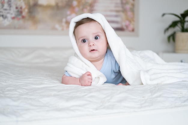 Nettes Baby 6 Monate alt im blauen Bodysuit lächelnd und liegend auf Bett mit weißem Plaid zu Hause.