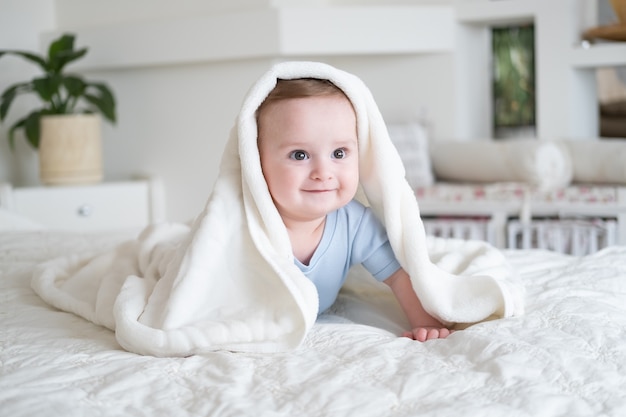 Nettes Baby 6 Monate alt im blauen Bodysuit lächelnd und liegend auf Bett mit weißem Plaid zu Hause.