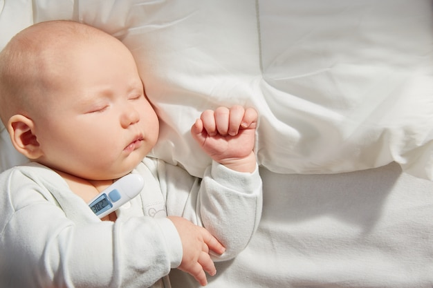 Nettes Baby, das auf einem Kissen mit einem Thermometer schläft. Messen Sie die Temperatur.