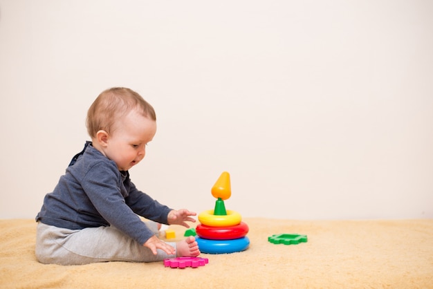 Nettes Baby, das mit bunter Spielzeugpyramide im hellen Schlafzimmer spielt.