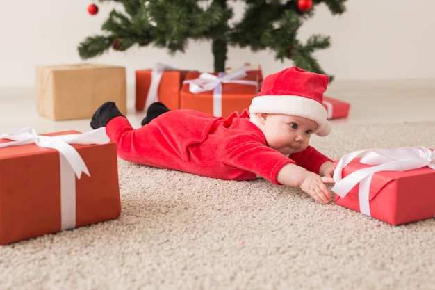 Nettes Baby, das Weihnachtsmannanzug trägt, der auf Boden über Weihnachtsbaum kriecht