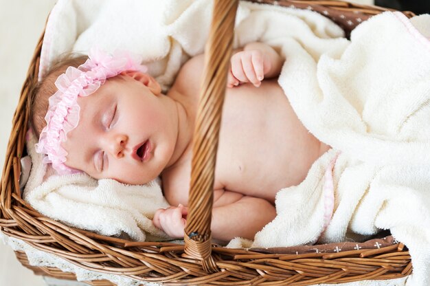 Nettes Baby in einem Korb. Blick von oben auf das kleine Baby, das schläft, während es im Weidenkorb liegt und mit einem Handtuch bedeckt ist