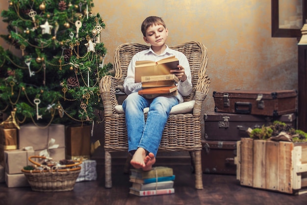 Nettes Baby in einem Stuhl, der ein Buch in einem weihnachtlichen Retro-Interieur liest