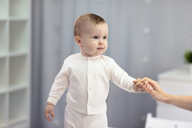 Nettes Baby in einem weißen Anzug, der in einem hellen Raum sitzt