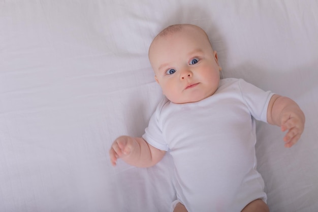 Nettes Baby in einem weißen Bodysuit, der im Bett mit Baumwollunterwäsche liegt, Draufsichtraum für Text