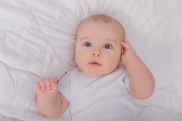 Nettes Baby in einem weißen Bodysuit, der im Bett mit Baumwollunterwäsche liegt, Draufsichtraum für Text