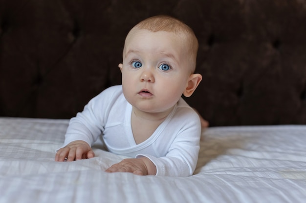 Nettes Baby in einem weißen hellen Body auf dem Bett zu Hause l