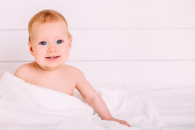 Nettes Baby mit blauen Augen, die in ein weißes Handtuch gewickelt werden.