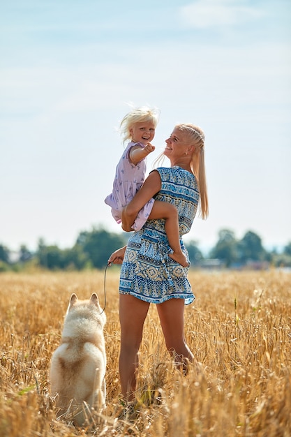 Nettes Baby mit Mutter und Hund auf Weizenfeld