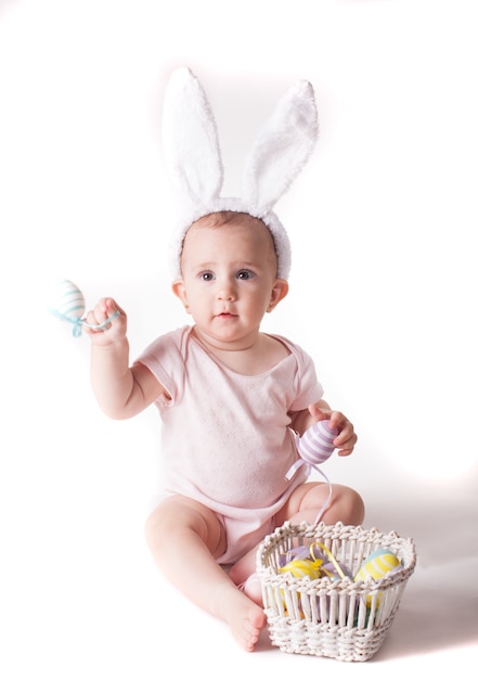 Nettes Babymädchen, das in einem gestrickten Kaninchenhut lokalisiert auf Weiß sitzt