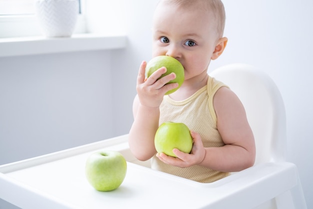 nettes Babymädchen im Kinderstuhl, der Äpfel isst Baby erste feste Nahrung