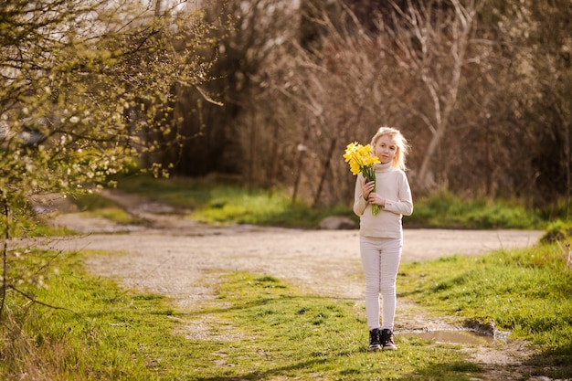 Nettes blondes glückliches kleines Mädchen mit gelbem Land der Narzissen im Frühjahr