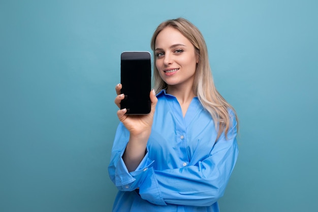 Nettes blondes Mädchen, das ein Smartphone mit einer Vorlage für eine Anwendung auf blauem Hintergrund hält