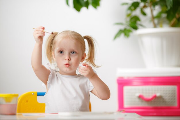 Nettes entzückendes Baby, das das Malen mit Wasserfarben lernt. Kleines Kleinkindkind, das zu Hause zeichnet, mit bunten Pinseln. Gesunde glückliche Tochter, die mit Farben, Wasser zu Hause oder im Kinderzimmer experimentiert