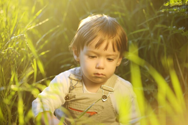 Nettes entzückendes Babykind, das im schönen grünen Gras sitzt