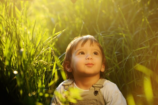 Nettes entzückendes Babykind, das im schönen grünen Gras sitzt