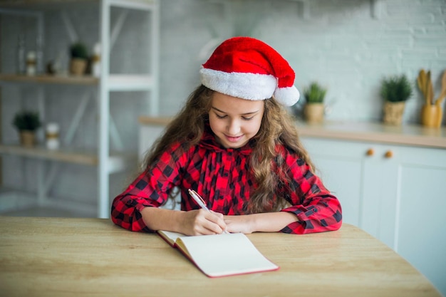 Nettes entzückendes lächelndes Mädchen in der Weihnachtsmannmütze zu Hause