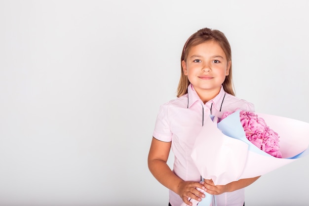 Nettes entzückendes Mädchen, das einen Blumenstrauß von rosa Blumen für Schullehrer der reizenden Mutter hält.