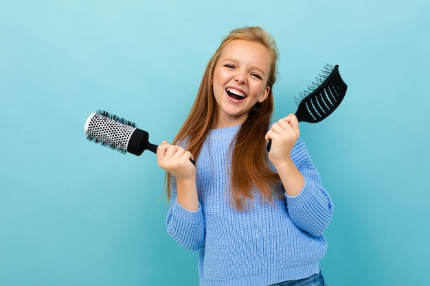 Nettes europäisches Mädchen, das einen Haarkamm auf hellblau hält