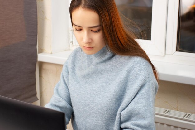 Nettes europäisches Mädchen zu Hause, das an einem Laptop sitzt, arbeitet, einkaufen geht