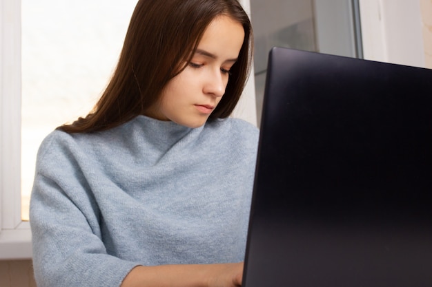 Nettes europäisches Mädchen zu Hause, das an einem Laptop sitzt, arbeitet, einkauft