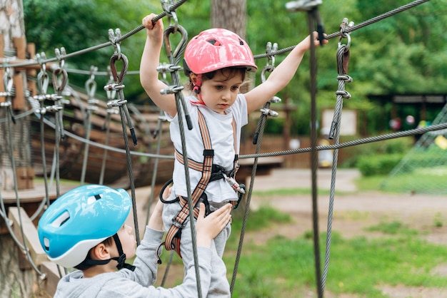 Nettes, fokussiertes, kleines Mädchen geht die Seilbahn und hält sich am Seil fest. Mädchen mit Schutzhelm und Versicherung