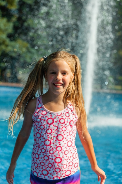Nettes fröhliches kleines Mädchen spielt im Brunnen. Das Kind hat Spaß in einem Sommerpark im Stadtbrunnen.
