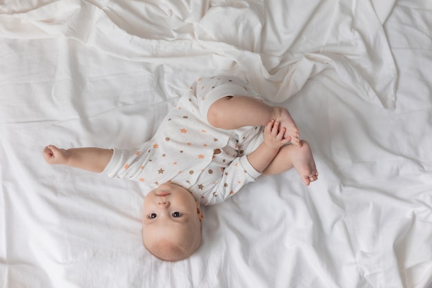 Nettes fröhliches Neugeborenes liegt auf dem Rücken auf einem weißen Blatt-Draufsicht-Lifestyle