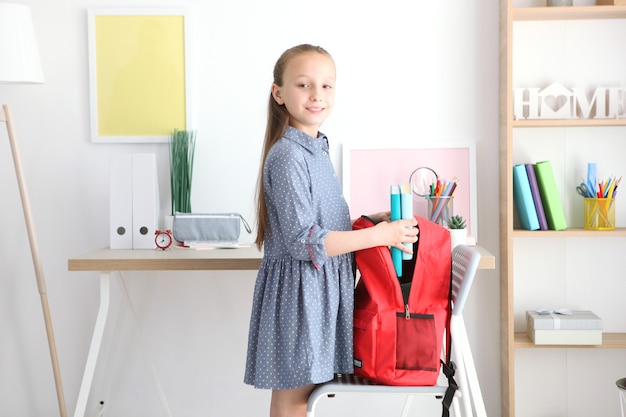 Nettes fröhliches Schulmädchen steckt Briefpapier in einen Rucksack