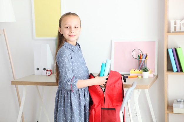 Nettes fröhliches Schulmädchen steckt Briefpapier in einen Rucksack