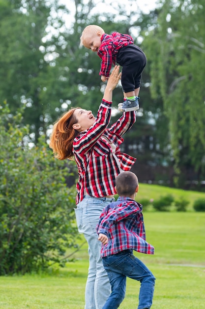 Nettes fröhliches zwei Jungenbruderkind mit Mutter spielen draußen im Park.