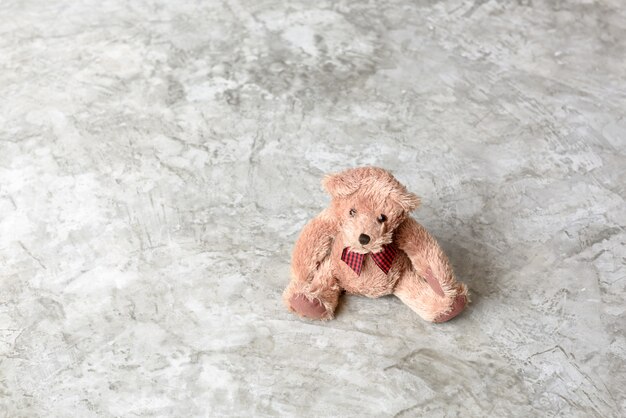 Nettes geschwollenes Teddybärspielzeug sitzen allein im Zementwandhintergrund