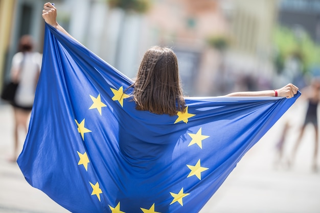 Nettes glückliches junges Mädchen mit der Flagge der Europäischen Union in den Straßen irgendwo in Europa.