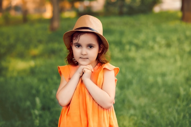 Nettes glückliches kleines Mädchen mit Hut, das sich auf der Parkwiese oder im Wald amüsiert Kinderblick auf die Kamera Picknick in der Natur